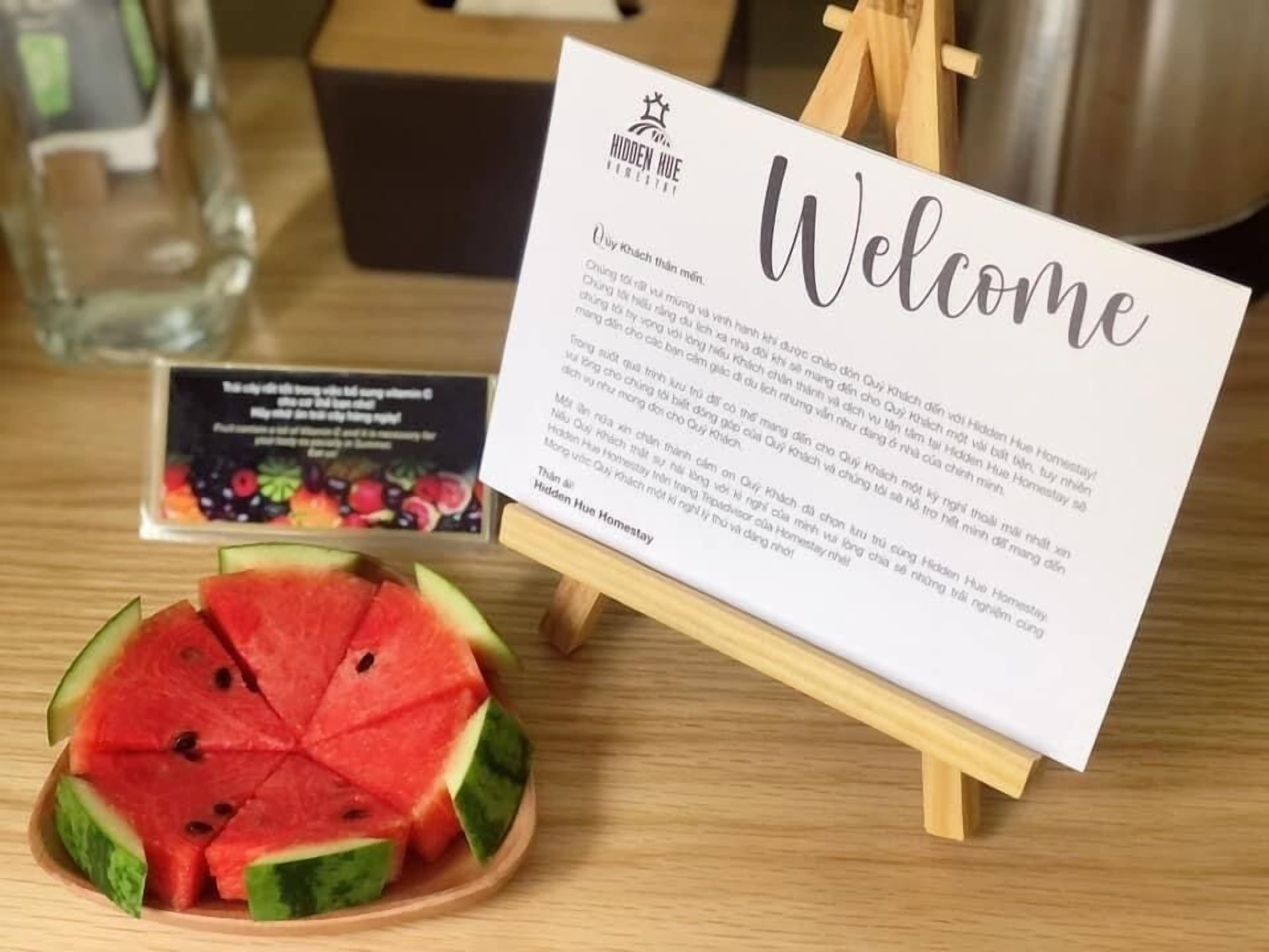 A welcome sign with text, a wooden easel, and a slice of watermelon on a table.