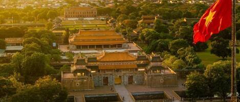 A traditional Vietnamese temple complex with a prominent flag, surrounded by lush greenery and a clear view of the cityscape in the background.