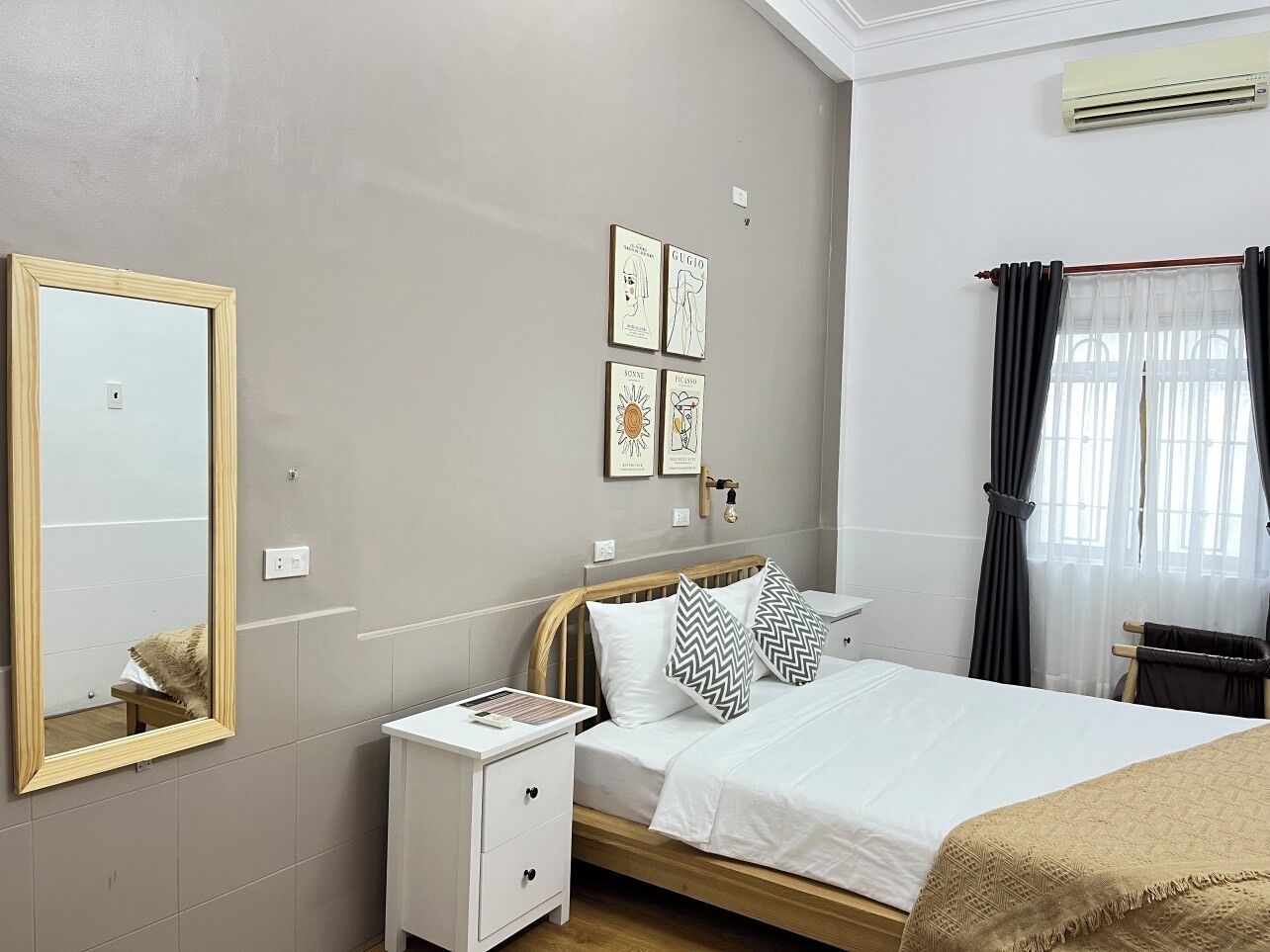 Une chambre à coucher avec un lit, une table de chevet et un miroir. Des œuvres d’art sont accrochées au mur au-dessus du lit.