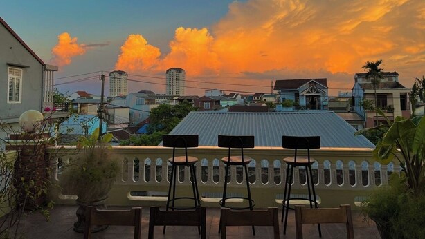 A balcony with three chairs, overlooking a cityscape during sunset. - Hidden Hue Homestay (Hue)