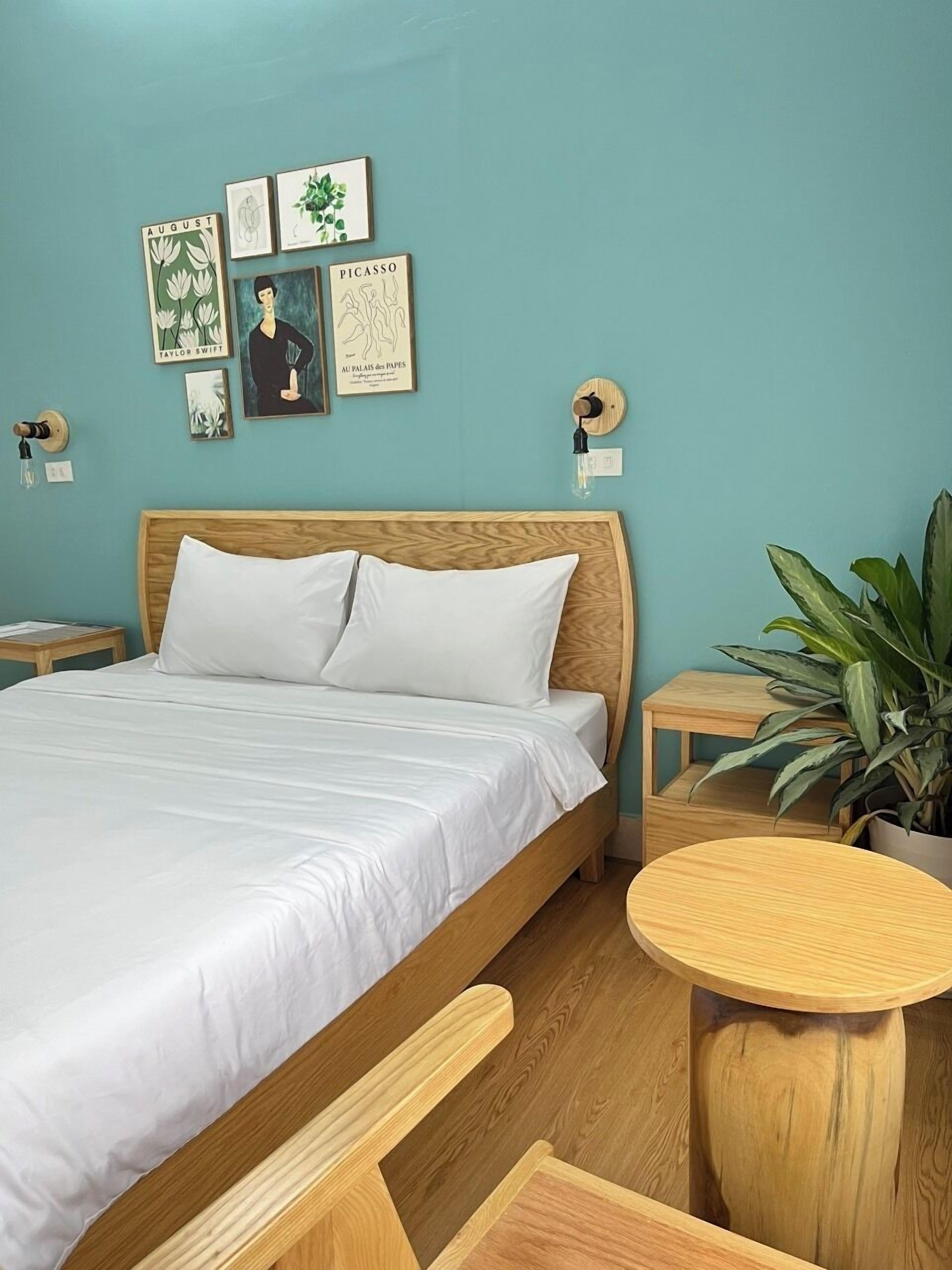 A bedroom with a wooden bed, white bedding, a round wooden table, and a potted plant.