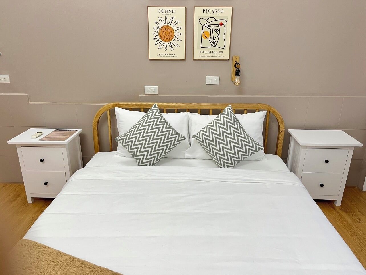 Un lit bien fait, avec deux oreillers, deux tables de chevet et deux œuvres d’art accrochées au mur.