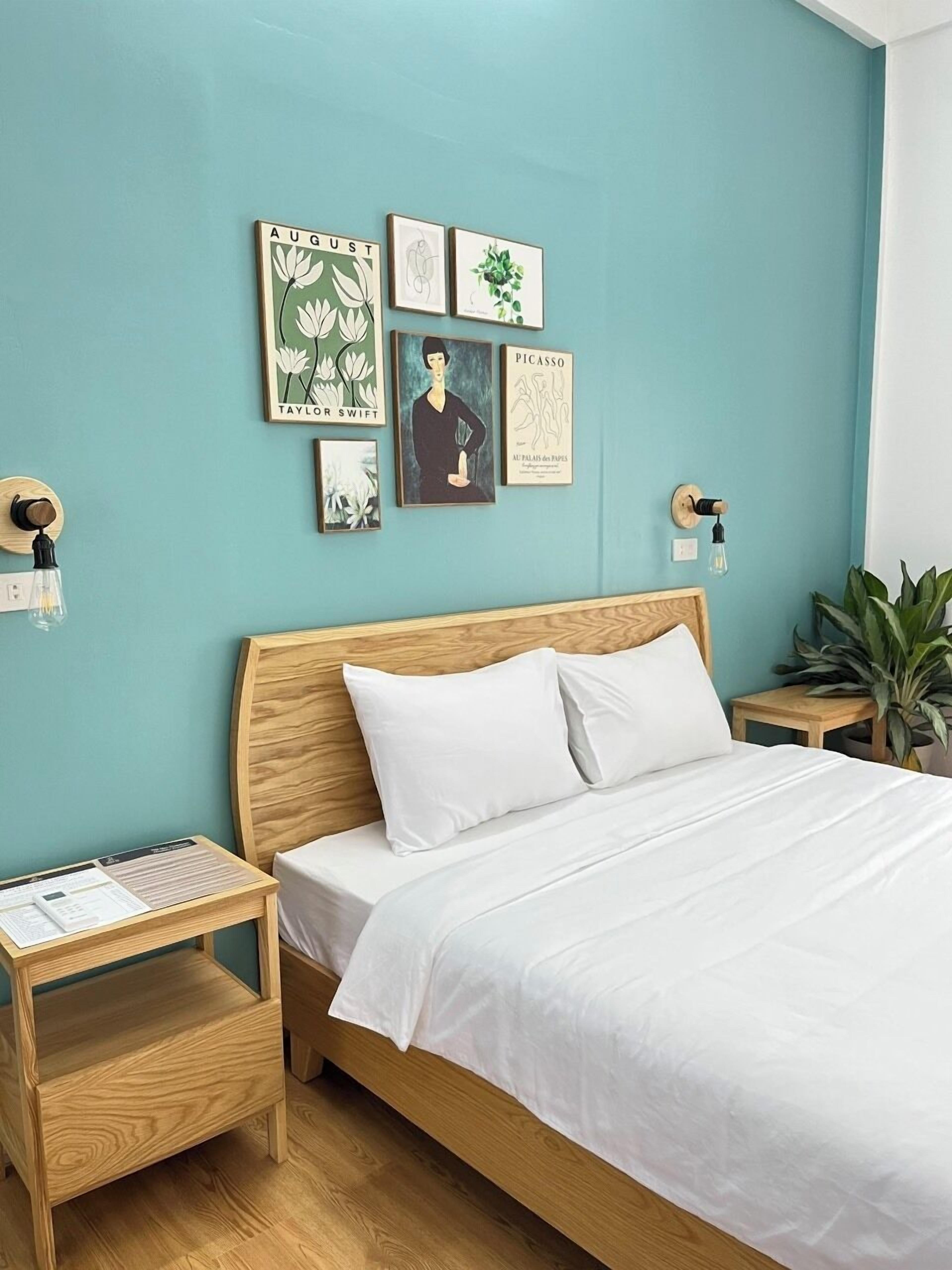 A neatly arranged bedroom with a wooden bed, white bedding, and a wall adorned with framed artwork including a Taylor Swift poster and a Picasso print.