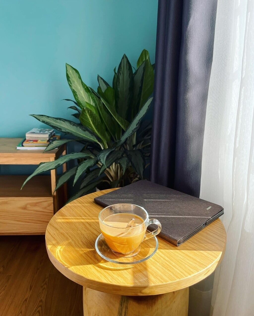 Una mesa redonda de madera con una taza de café de vidrio y un libro.