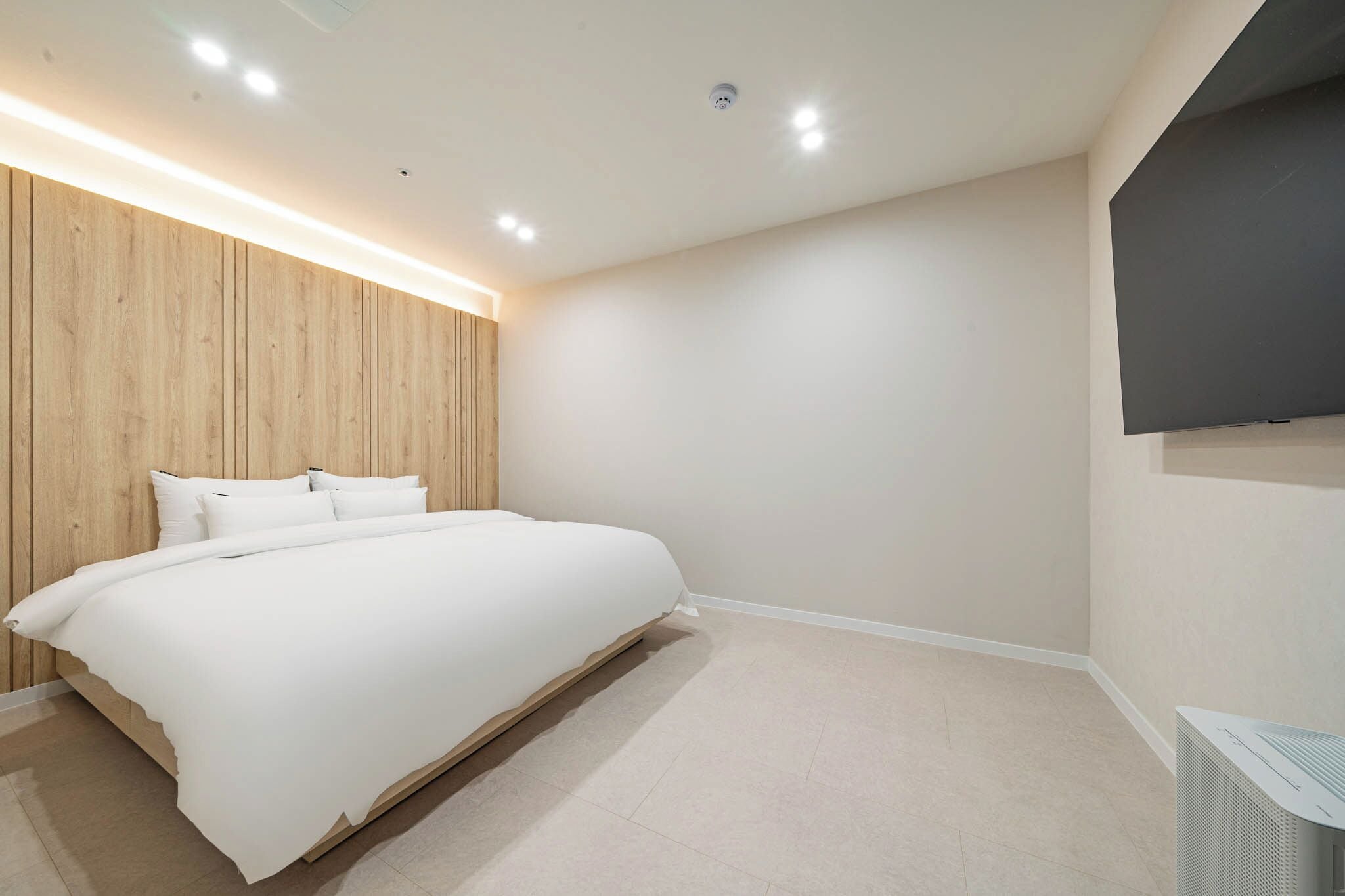 A bedroom with a bed, wooden panel wall, white bedding, and a flat-screen TV mounted on the wall.