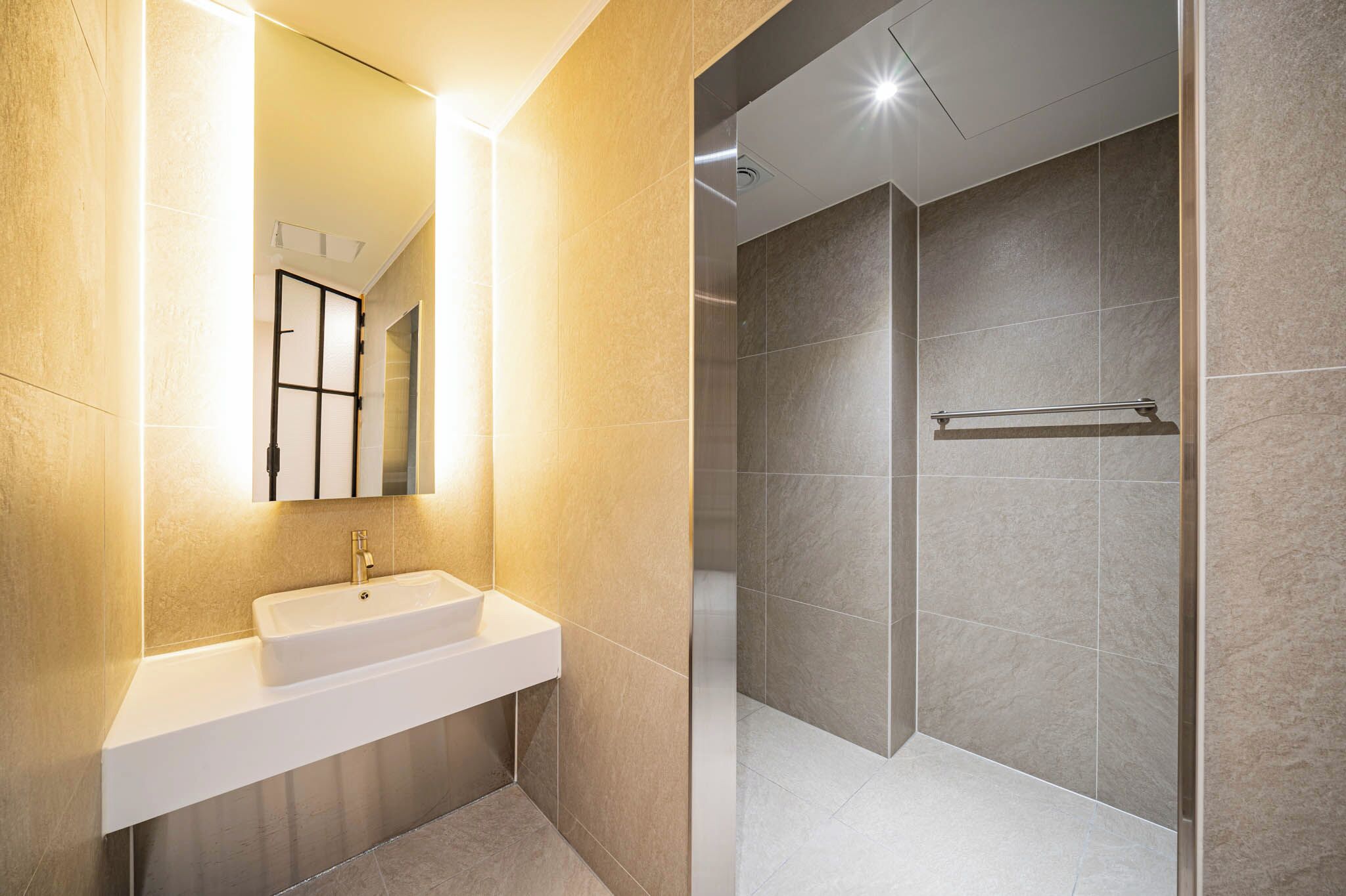 A modern bathroom with a white sink, a mirror, and a shower area with a glass door.