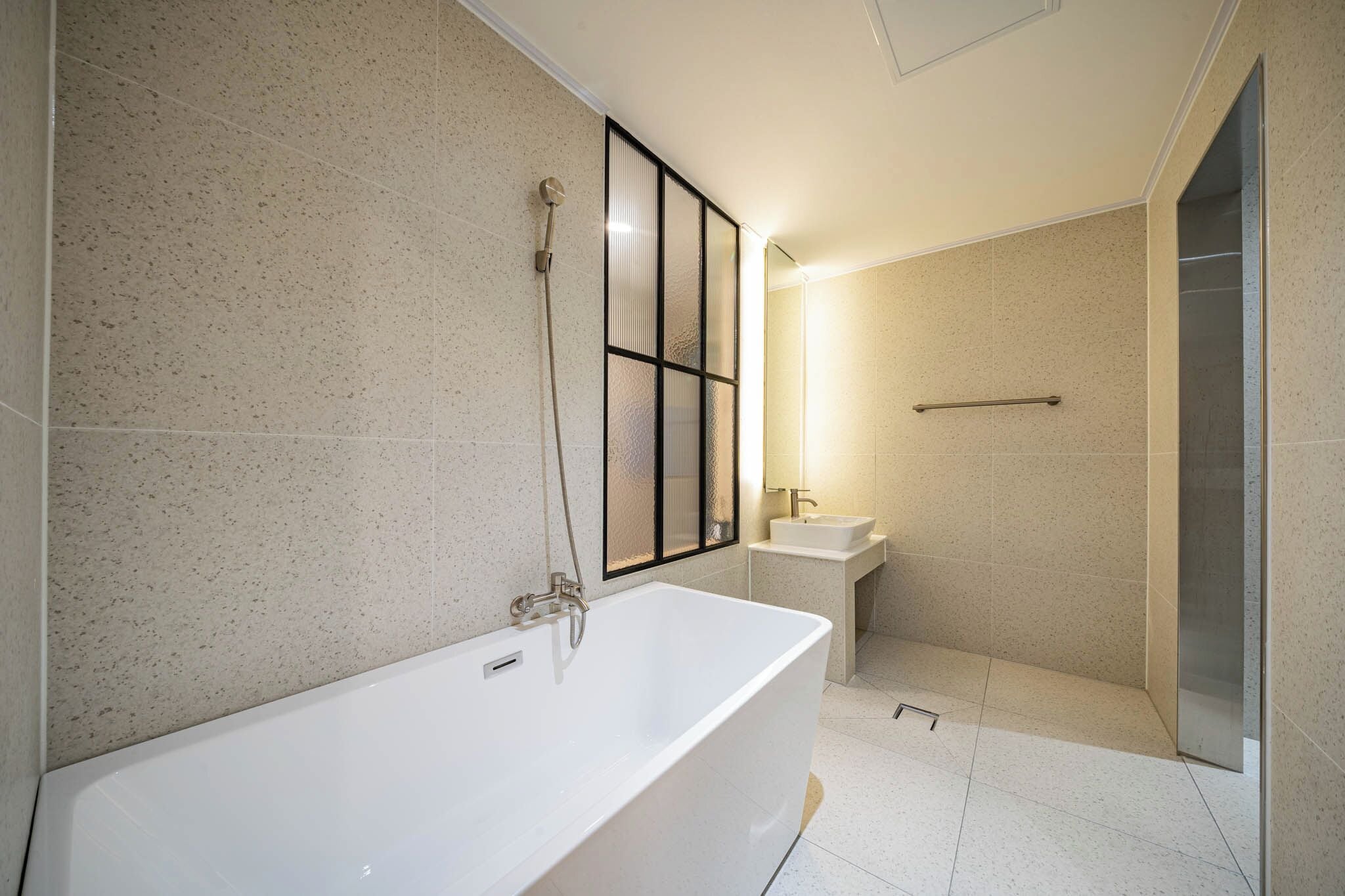Un baño moderno con una bañera independiente, mampara de ducha de vidrio y un lavamanos pequeño.