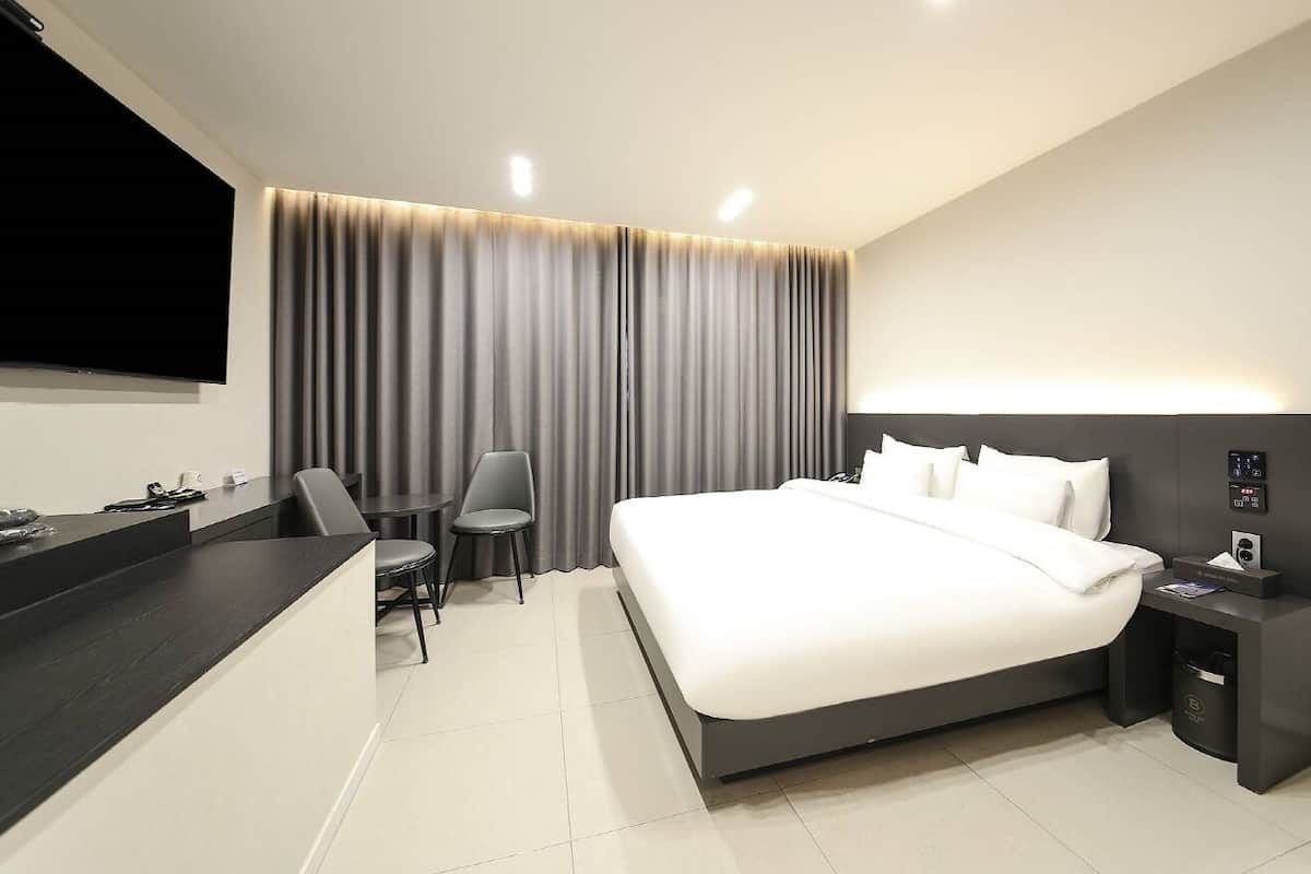 A modern hotel room with a large bed, a desk, and a TV.