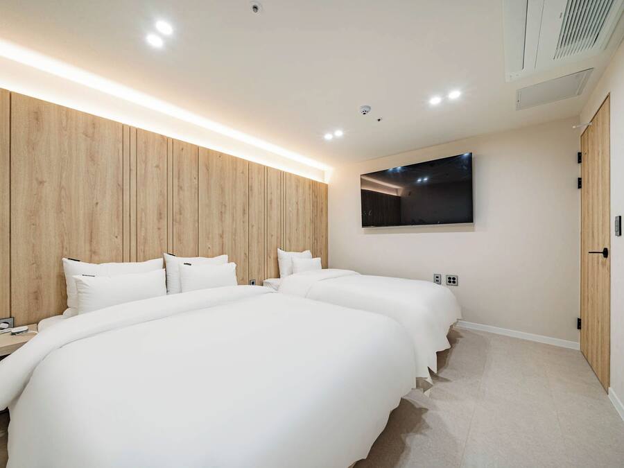 A modern hotel room with a large bed, bedside tables, a flat-screen TV, and wooden paneling on the wall.