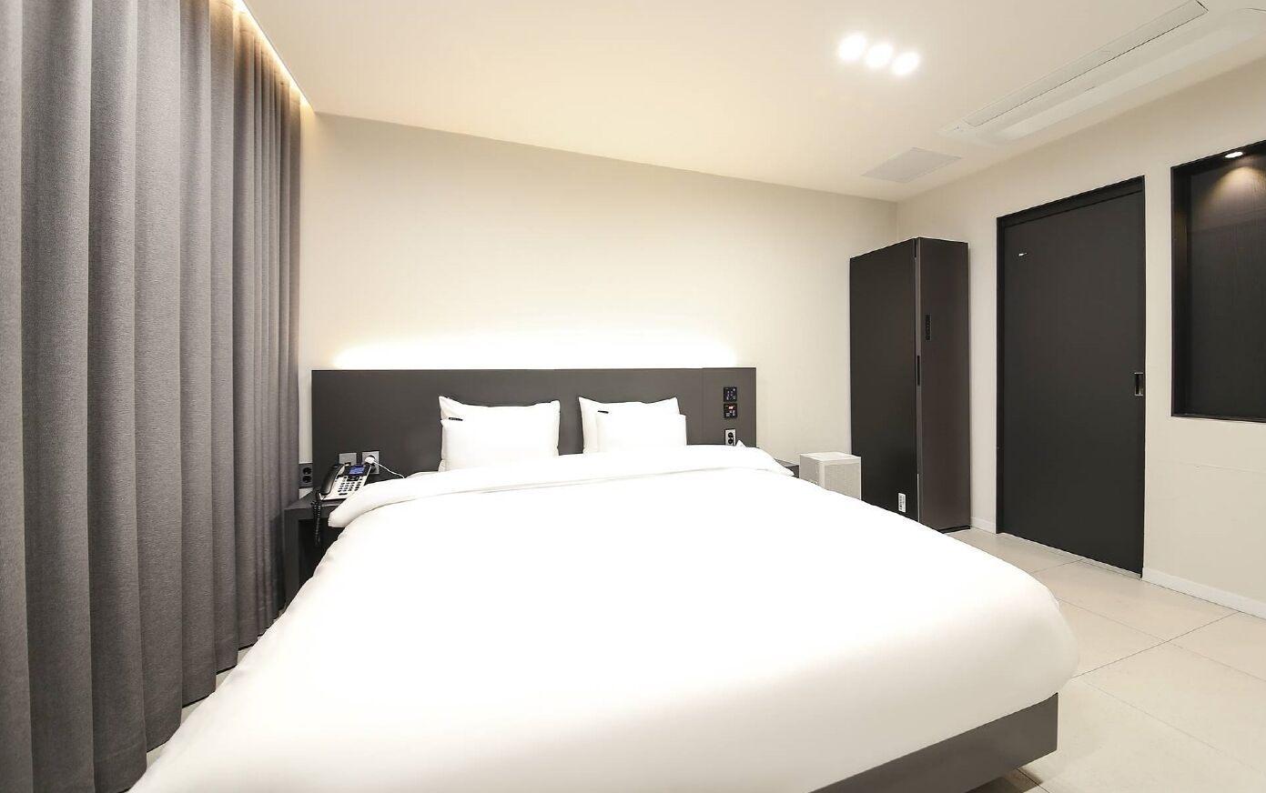 Ein modernes Hotelzimmer mit einem großen Bett, einem Nachttischtelefon und einem Kleiderschrank.