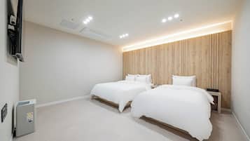 Una habitación de hotel moderna con dos camas, un cabecero de madera, un televisor de pantalla plana en la pared y una mesita de noche con una lámpara.