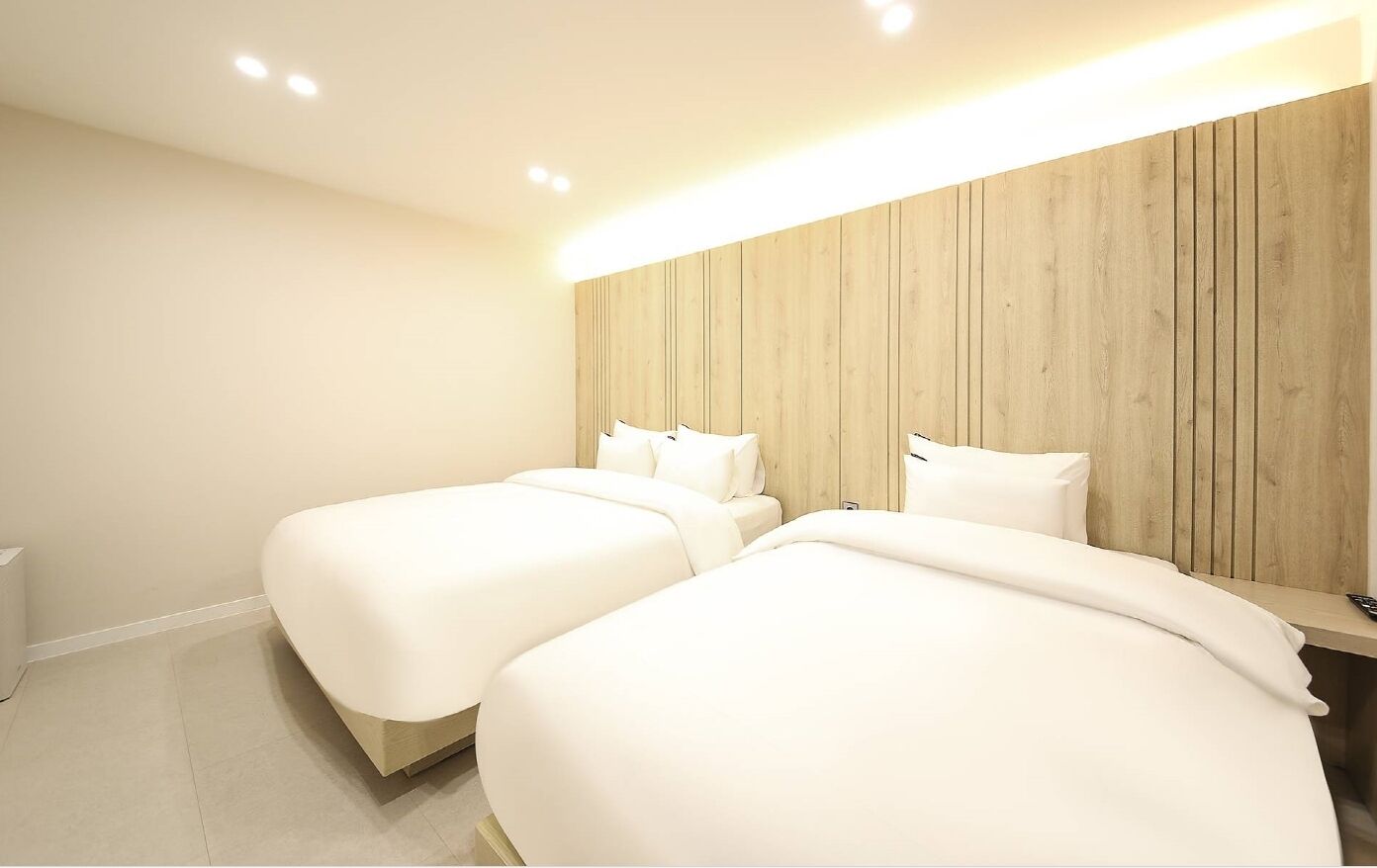 Una habitación de hotel con dos camas, un cabecero de madera y suelo blanco.