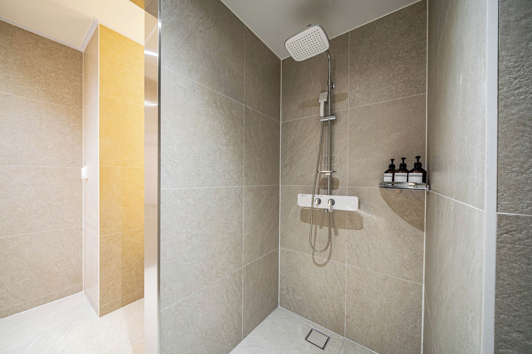 A modern shower with a handheld showerhead and a wall-mounted control panel.