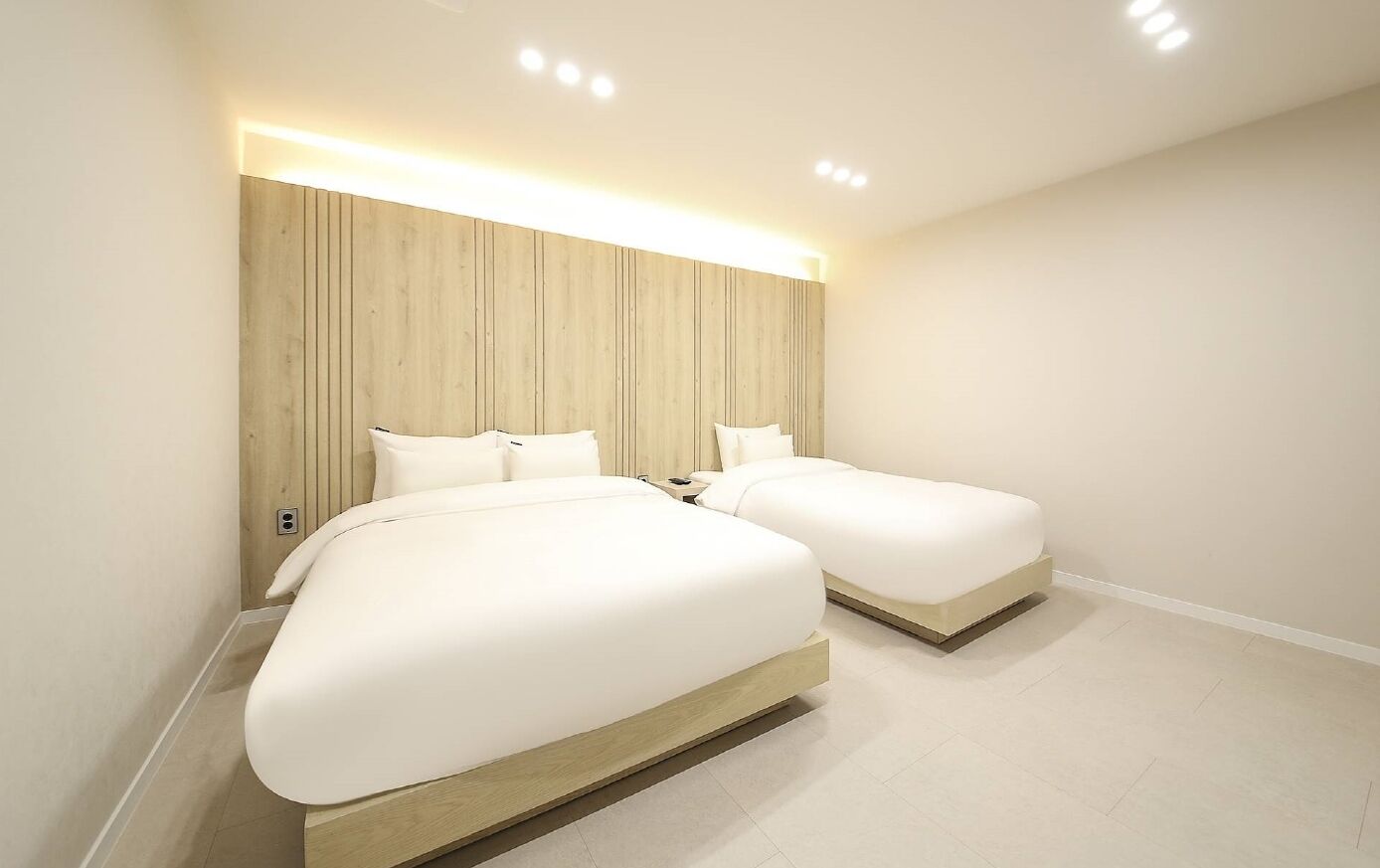 A modern hotel room with two beds, a wooden headboard, and recessed ceiling lighting.
