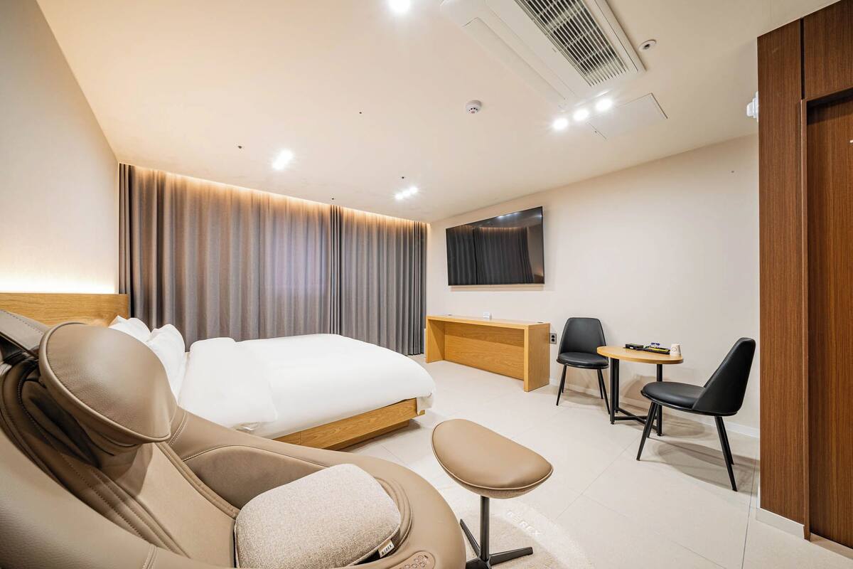 A modern hotel room with a large bed, a sofa, a desk, and two chairs.