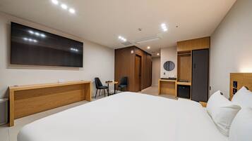 Una habitación de hotel moderna con una cama grande, un escritorio de madera, un televisor de pantalla plana, un armario y una pequeña zona de estar.