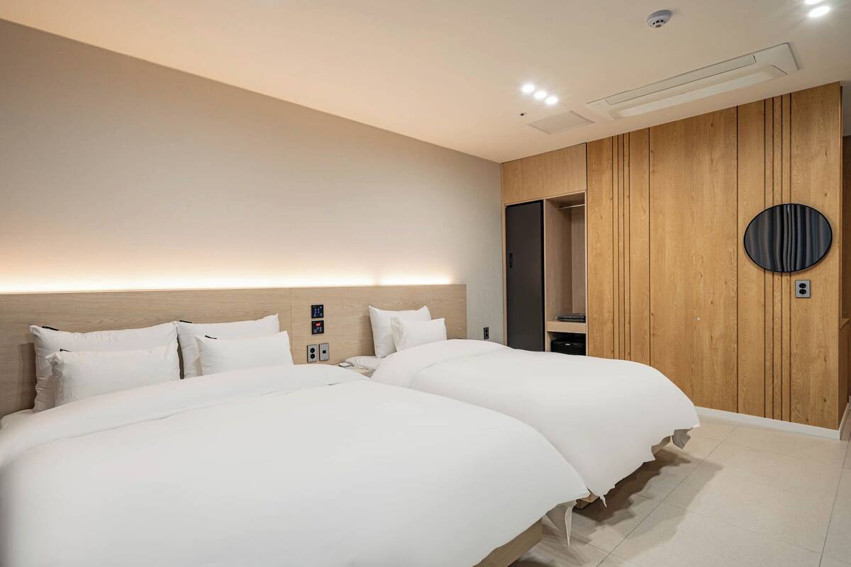 A modern hotel room with two large beds, a wooden accent wall, a round mirror, and a built-in wardrobe.