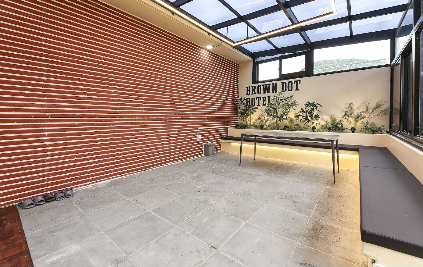 A hotel lobby with a red brick wall, a reception desk, and a large window with a view of greenery.