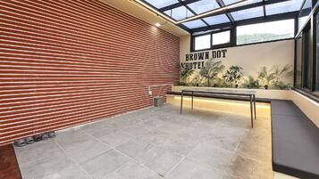A hotel lobby with a red brick wall, a reception desk, and a large window with a view of greenery.