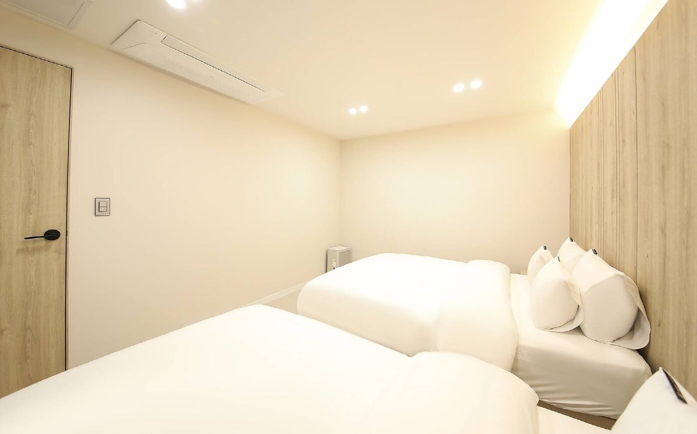 A hotel room with two beds, a wooden wardrobe, a bedside table, and a wall-mounted heater.