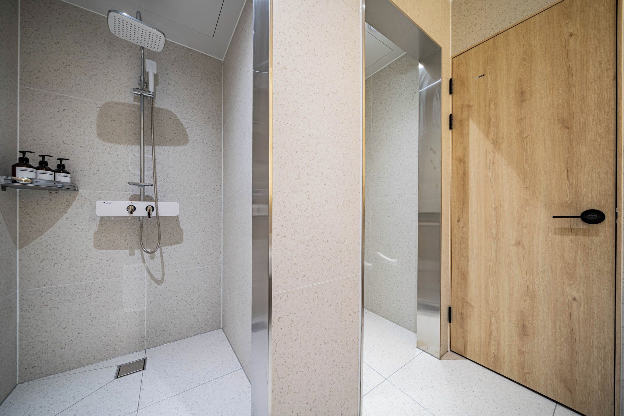 Ein modernes Badezimmer mit Dusche, Holztür und Fliesenboden.
