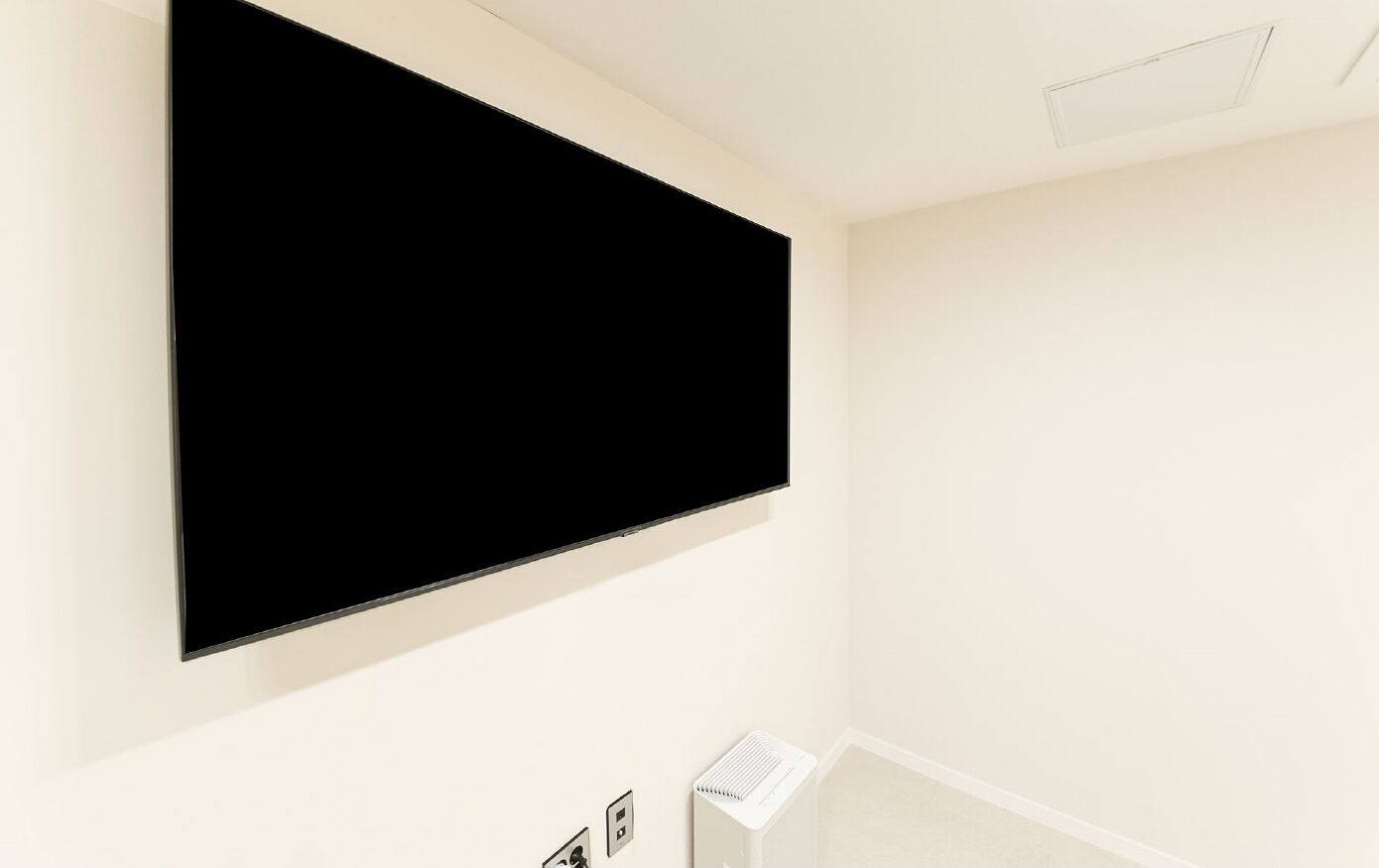 A room with a mounted flat-screen TV, a white air purifier, and a power outlet on the wall.