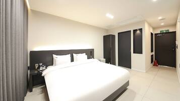 Habitació d'hotel moderna amb un llit gran, taules de nit, un telèfon i una porta amb un senyal verd.