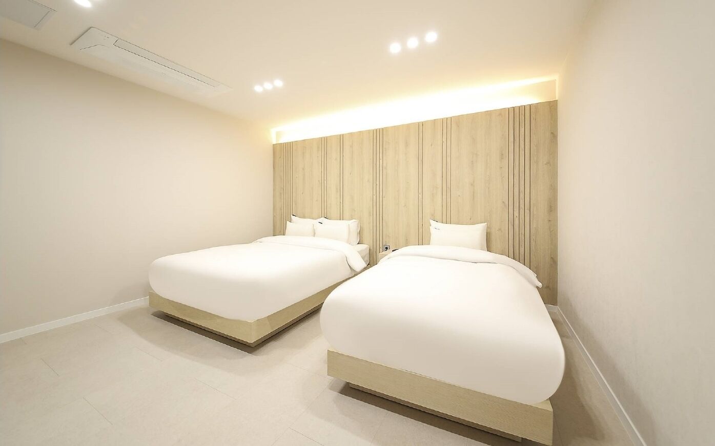 A modern hotel room with two beds, a wooden headboard, and recessed ceiling lighting.