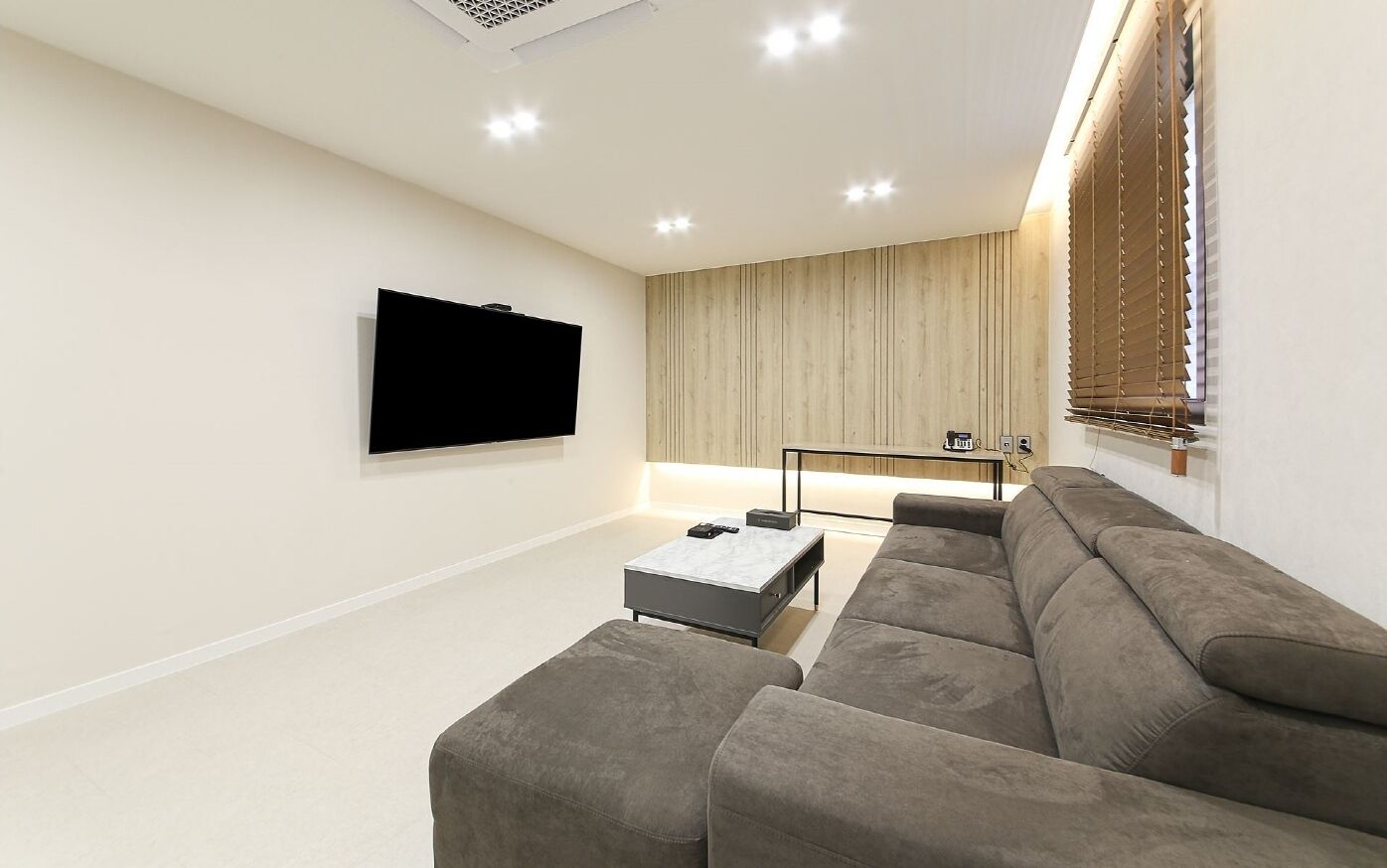 Un salon moderne avec un canapé d’angle, un téléviseur à écran plat fixé au mur, une table basse et un meuble télé intégré.