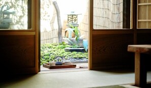 Una habitación japonesa tradicional con suelo de tatami, puerta corredera de shoji y un pequeño jardín visible a través de la puerta.