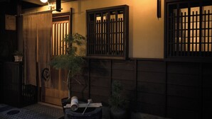 A traditional Japanese building with wooden sliding doors, a potted plant, and a lantern. - Kokonoe Machiya (Kyoto)