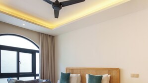Une chambre d’hôtel moderne dotée d’un grand lit, d’un ventilateur de plafond, d’une tête de lit en bois et offrant une vue sur l’extérieur.