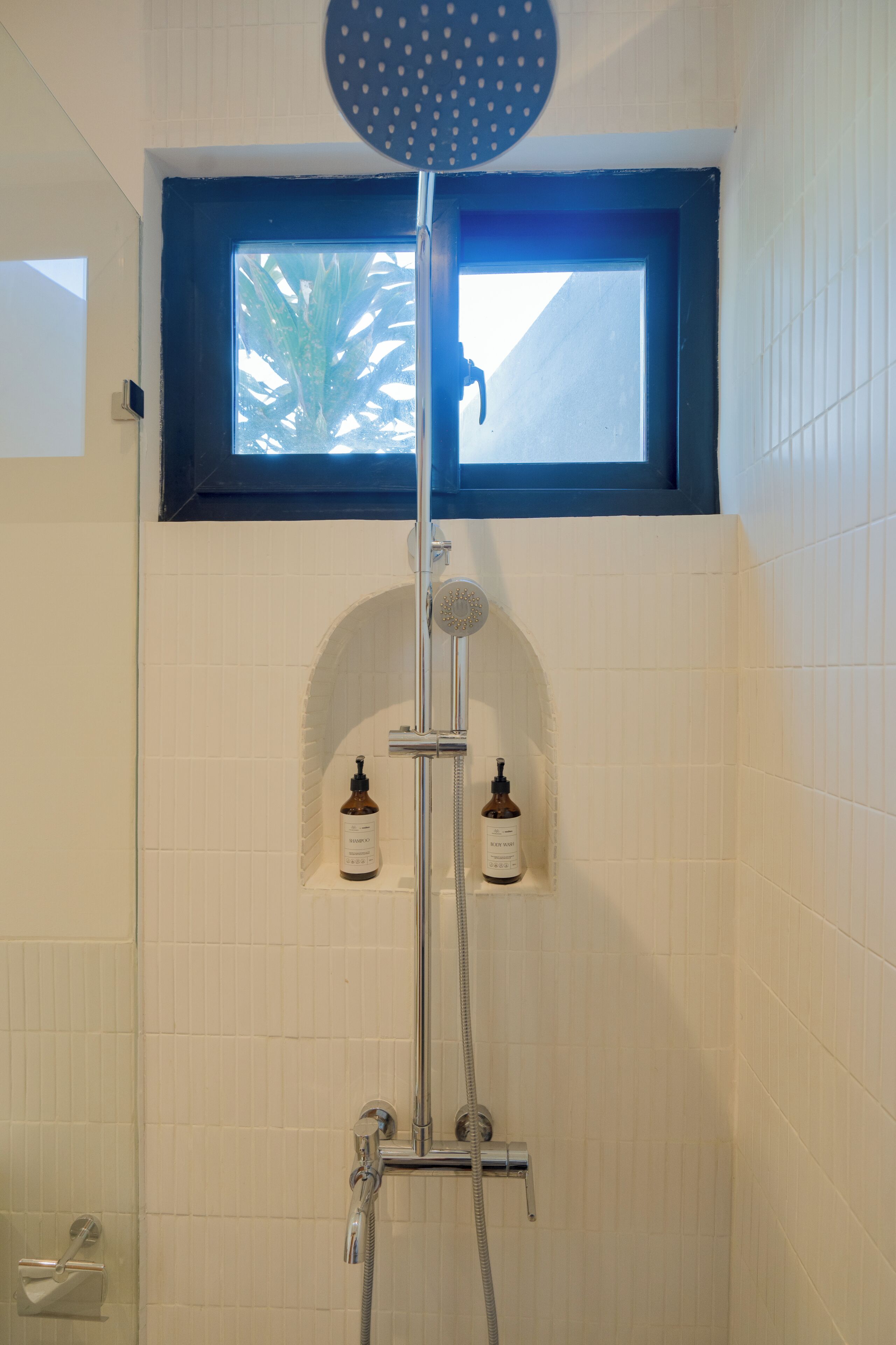 A shower with a handheld showerhead, a wall-mounted faucet, and a window above.