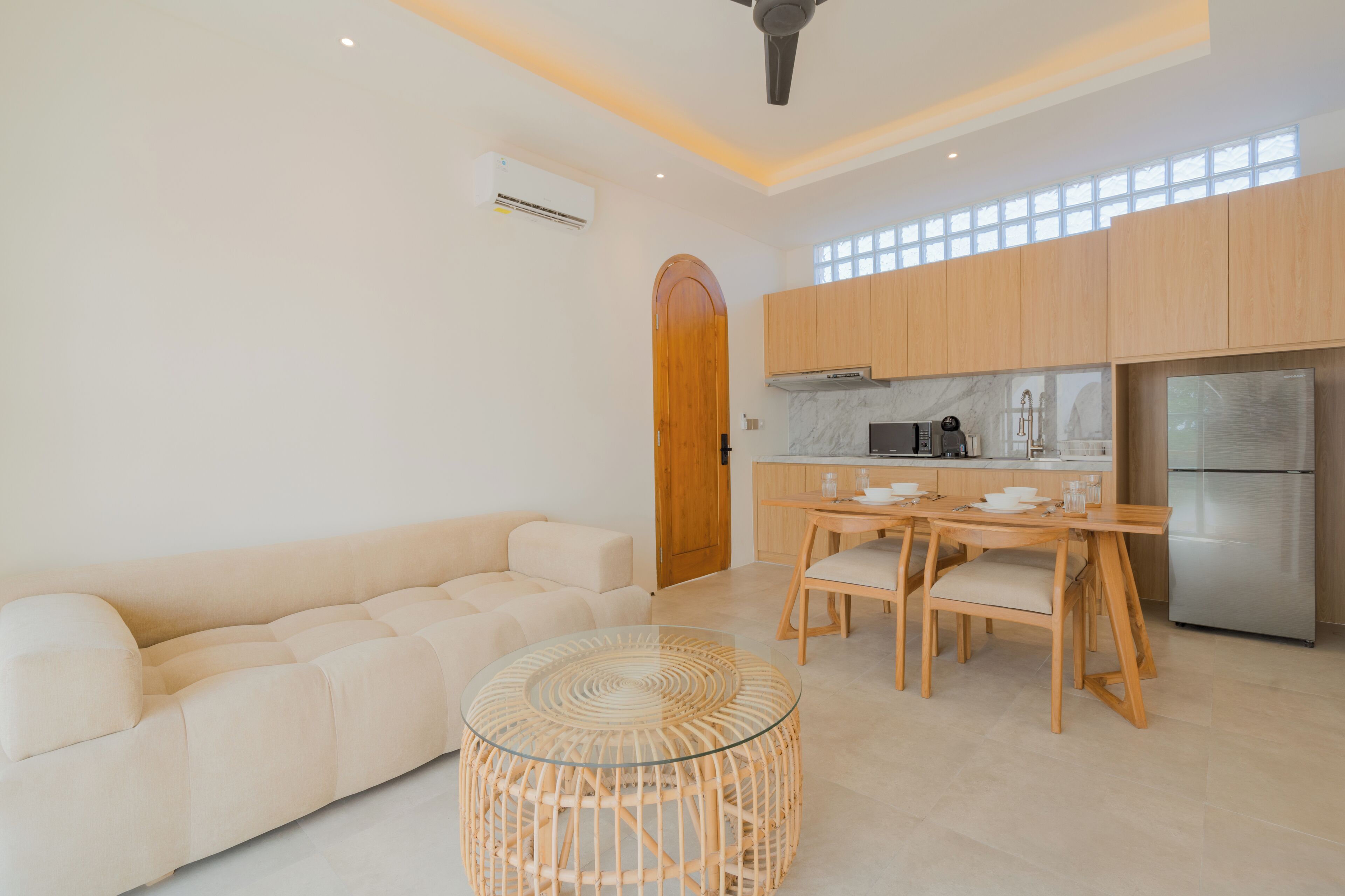 A modern kitchen with wooden cabinets, a stainless steel refrigerator, and a dining area with a glass table and chairs.