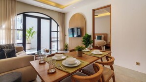 Un espace repas moderne avec une table en bois dressée pour quatre personnes, un canapé et un téléviseur fixé au mur.