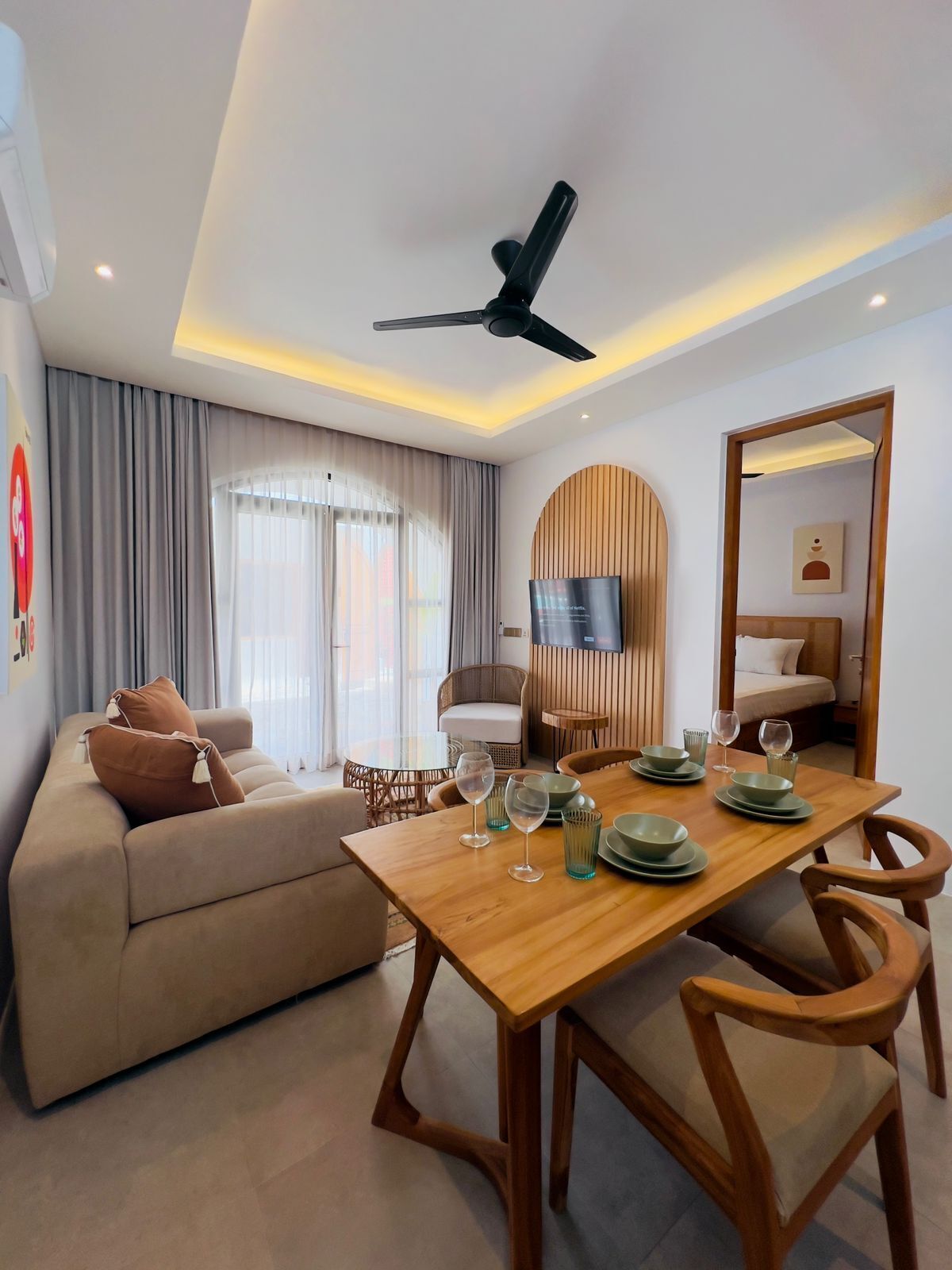 A modern living room with a wooden dining table, beige sofa, and a ceiling fan.