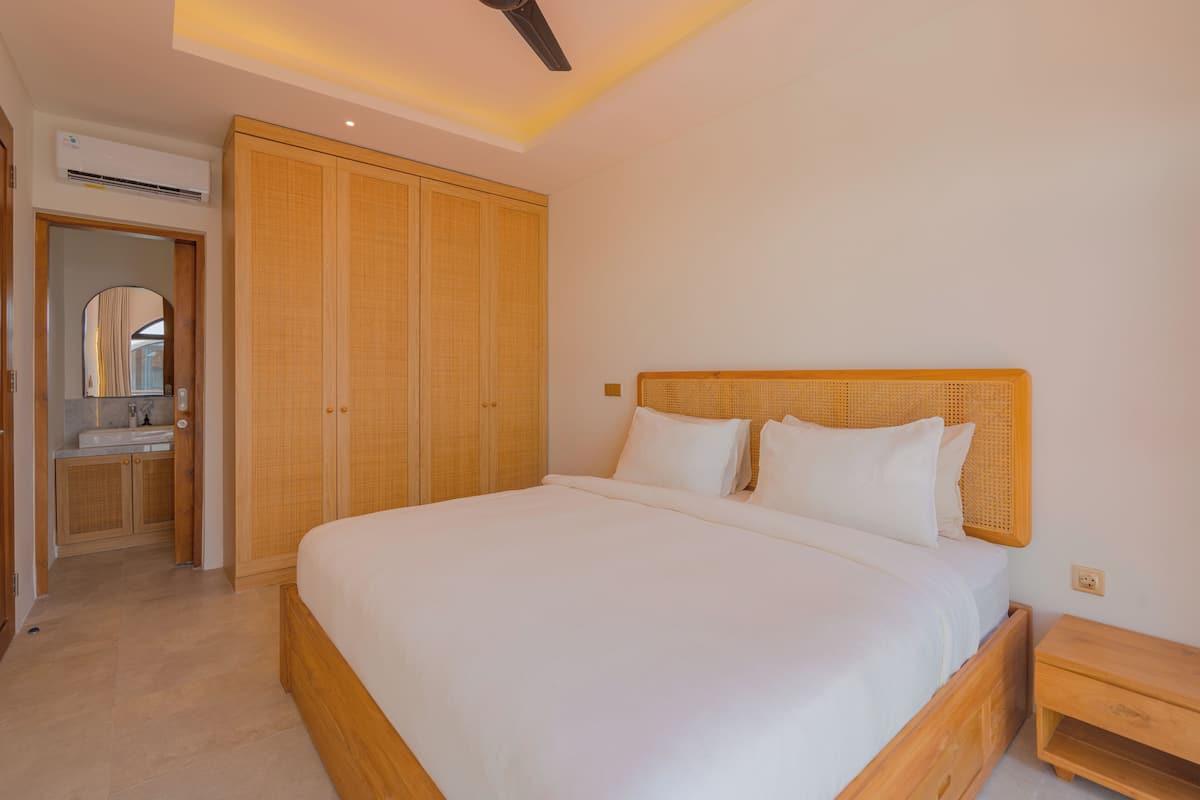 A bedroom with a large bed, wooden wardrobe, and a small bedside table.