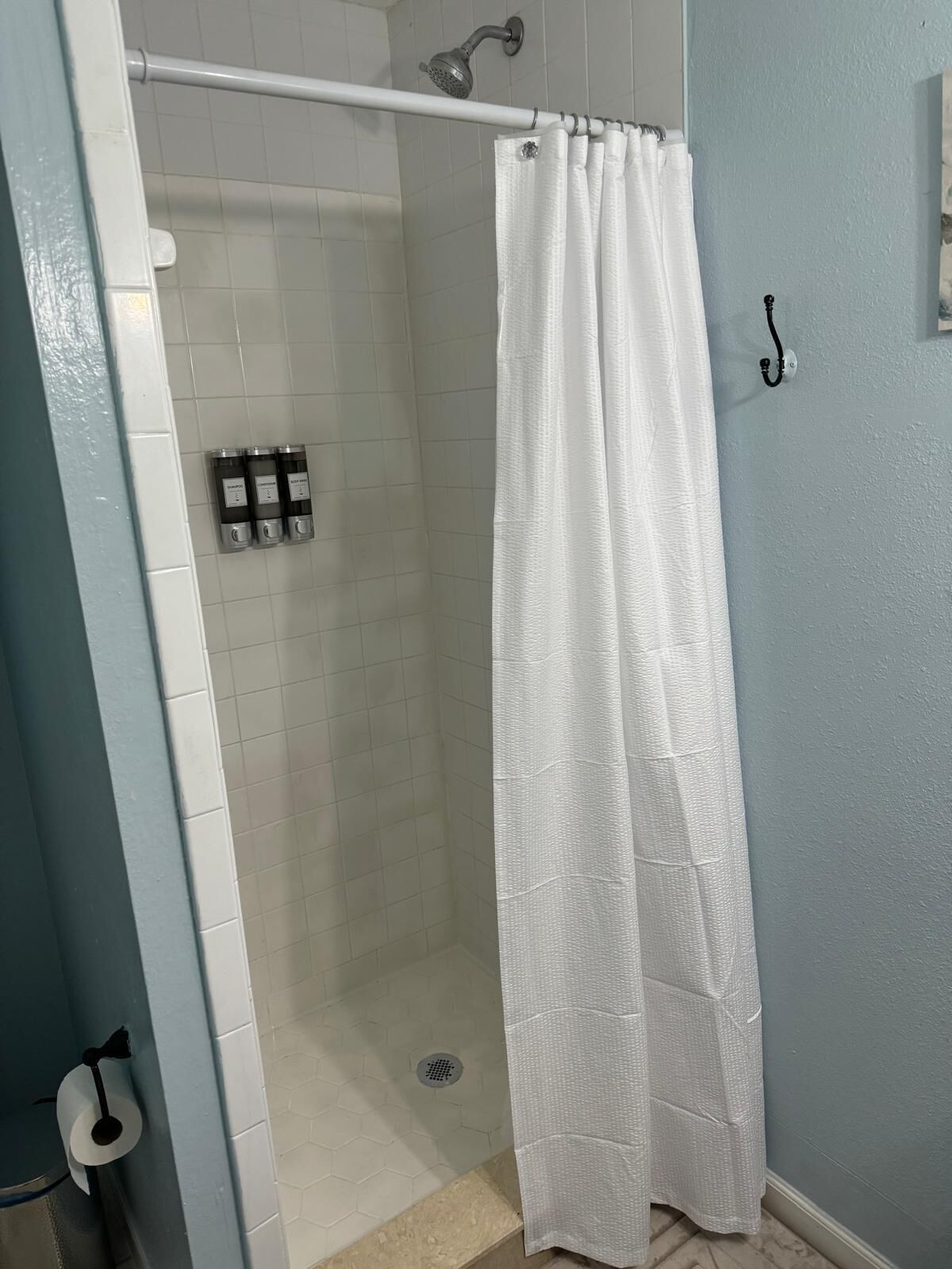 A shower area with a white shower curtain, a handheld showerhead, and a wall-mounted soap dispenser.