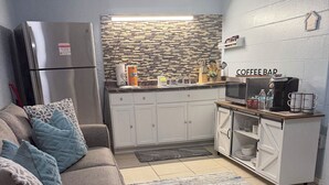 Un espace de vie compact comprenant un coin cuisine, un canapé agrémenté de coussins à motifs et un espace dédié à la préparation du café.