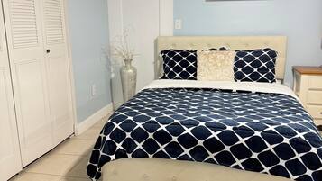 A bedroom with a bed, a nightstand, a vase with plants, a door, and a painting on the wall.