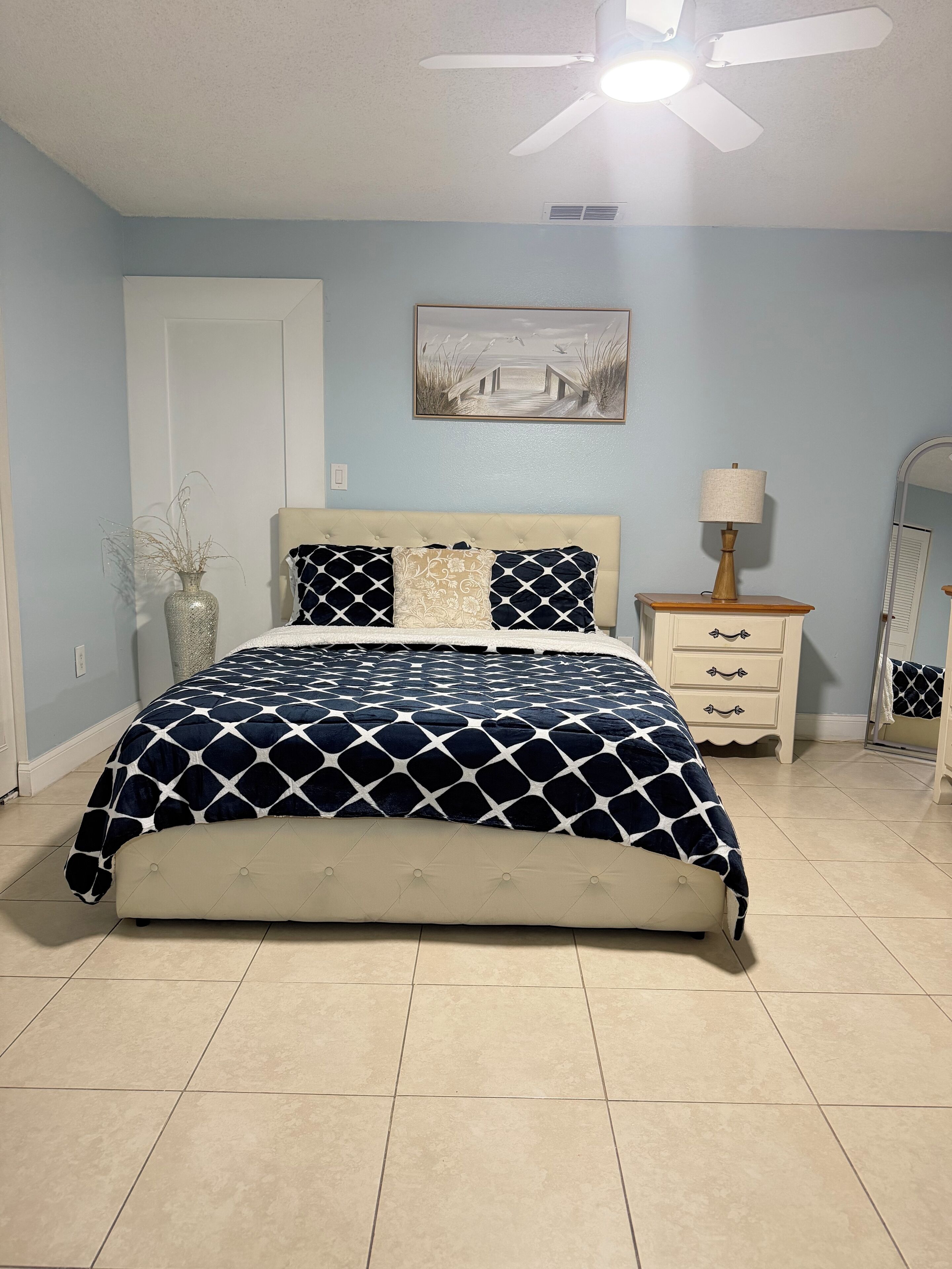 A bedroom with a bed, a nightstand, a lamp, a mirror, and a painting on the wall.