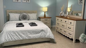Une chambre à coucher comprenant un lit, des tables de chevet, une commode, un ventilateur de plafond et des œuvres d’art murales.