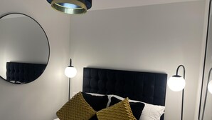 A modern bedroom with a tufted headboard, a round mirror, and two bedside lamps. - Modern-luxury 1bedroom-EnsuiteBathroom-Garden-Wifi (Basildon)
