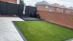 A backyard with a well-maintained lawn, a patio area with seating, and a brick wall. - Modern-luxury 1bedroom-EnsuiteBathroom-Garden-Wifi (Basildon)