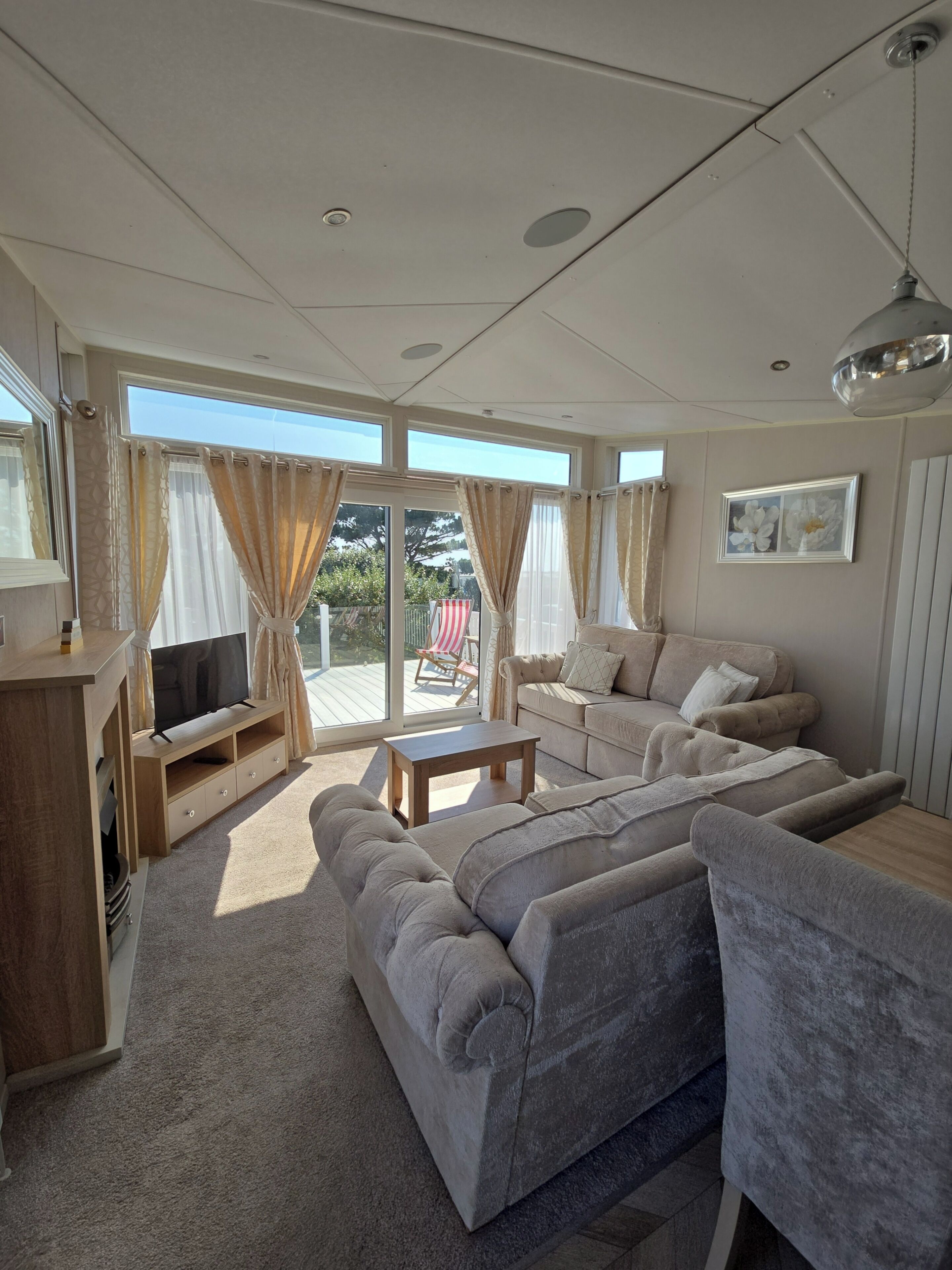 A spacious living room with a sofa set, a television on a wooden stand, and a ceiling fan.
