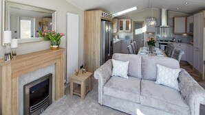 A modern living room with a fireplace, a grey sofa, and a dining area with a table and chairs. - 2Br Lodge - Pool - Fireplace - PetsOK - Parking (Newquay)