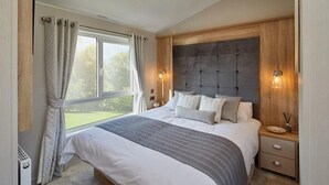A bedroom with a large bed, a wooden headboard, two bedside tables, and a window with curtains. - 2Br Lodge - Pool - Fireplace - PetsOK - Parking (Newquay)