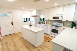 Una cocina moderna con armarios blancos, una isla central, un microondas, un horno y un lavaplatos.