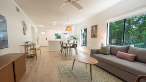 Un salon moderne avec un canapé, une table à manger et des chaises. On aperçoit une cuisine à l’arrière-plan, avec un coin repas.