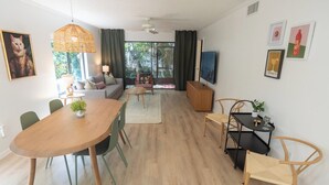 Un salon moderne avec une table à manger en bois, des chaises vertes, un canapé, un téléviseur et des œuvres d’art accrochées aux murs.
